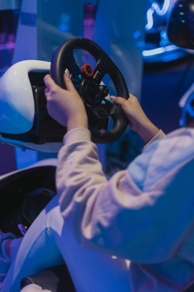 Close-up of hands holding a racing wheel in a virtual reality gaming setup indoors.